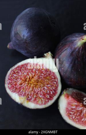 Primo piano di fichi viola scuro freschi, alcuni interi e altri a fette, con texture e semi dettagliati Foto Stock
