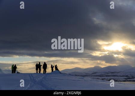 Silhouette, turisti retroilluminati in attesa del tramonto sulla montagna Storsteinen, Tromso, Troms og Finnmark, Norvegia Foto Stock