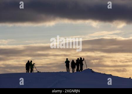 Silhouette, turisti retroilluminati in attesa del tramonto sulla montagna Storsteinen, Tromso, Troms og Finnmark, Norvegia Foto Stock