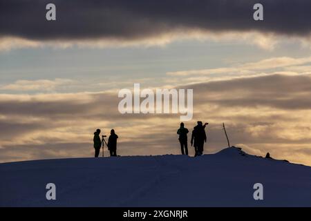 Silhouette, turisti retroilluminati in attesa del tramonto sulla montagna Storsteinen, Tromso, Troms og Finnmark, Norvegia Foto Stock