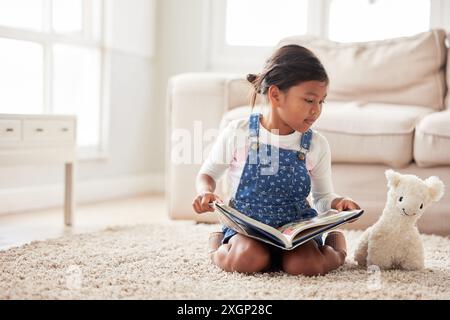 Giocattolo, gioco e libro di lettura per bambini a casa per imparare, fingere e conoscere insieme sul pavimento. Educazione, orsacchiotto e storie di ragazza su tappeto Foto Stock