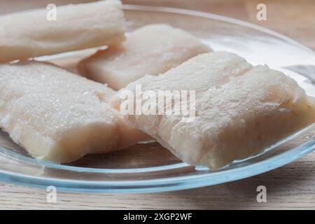 I filetti di eglefino congelati si scongelano su una piastra di vetro. Su sfondo di un tagliere di legno Foto Stock