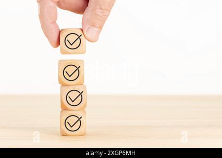 Concetto di controllo o lista di controllo. Blocco cubo di legno selezionato a mano con icona di controllo accatastata su un tavolo di legno. Spazio di copia Foto Stock