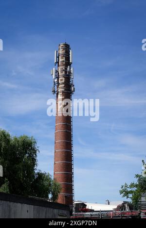 Colonia, Germania 09 luglio 2024: Trasmettitori radio mobili su un vecchio camino industriale a colonia Ehrenfeld di fronte a un cielo blu con nuvole di velo Foto Stock