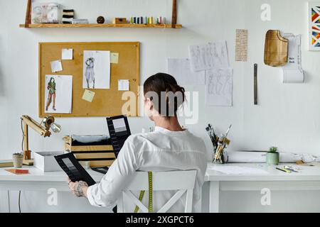 Un giovane, che lavora nel suo atelier di restauro di abiti, esamina attentamente i campioni di tessuto mentre è seduto alla sua scrivania. Foto Stock