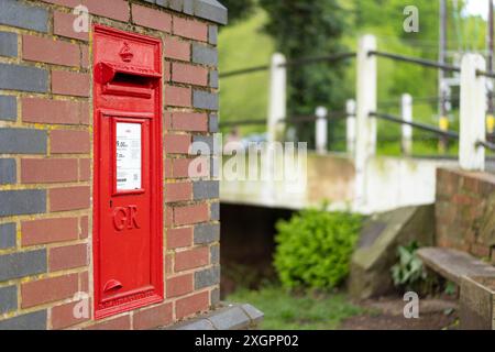 Primo piano di una cassetta postale rossa della Royal mail/lettera con le lettere cifrate reali GR sul davanti, incastonata in una tradizionale parete di mattoni all'aperto, Regno Unito. Foto Stock