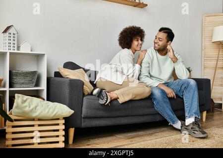 Una giovane coppia afroamericana usa il linguaggio dei segni per comunicare mentre si siede su un divano in casa. Foto Stock