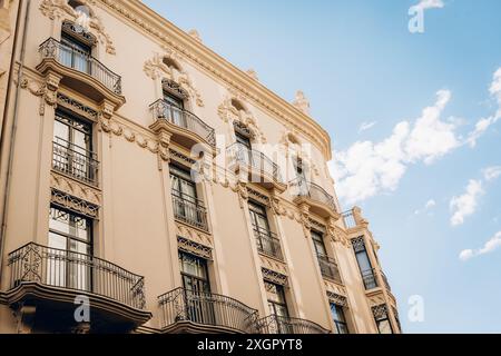 Vista dall'angolo basso di un elegante edificio storico di Valencia con balconi ornati e dettagli architettonici che catturano la bellezza del patrimonio spagnolo sotto un cielo limpido. Foto Stock