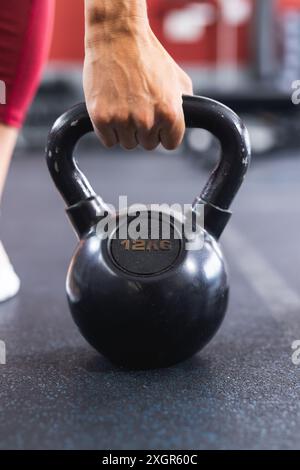 Primo piano di una mano in forma afferrando un campanello da 12 kg in palestra. Concentrandosi sull'allenamento di forza e sul fitness, l'immagine cattura un momento di allenamento. Foto Stock