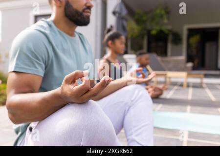 Il giovane uomo birazziale medita all'aperto, con spazio di copia. La famiglia ama una tranquilla sessione di yoga insieme a casa. Foto Stock