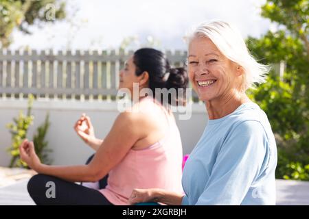 Amici anziani felici e diversi che praticano la meditazione yoga seduti nel giardino soleggiato. Posizione Lotus, yoga, benessere, meditazione, amicizia e lui Foto Stock