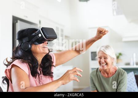 Due amiche anziane felici e diverse che ridono e utilizzano il visore vr a casa. Amicizia, tecnologia, interfaccia digitale, comunicazione, pensionamento, d Foto Stock