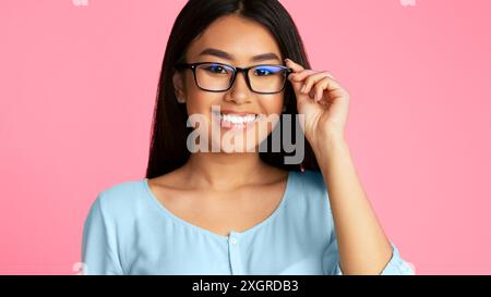 Sorridente giovane donna che indossa occhiali su sfondo rosa Foto Stock