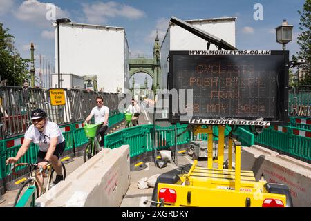 Ciclisti che utilizzano una pista ciclabile temporanea per attraversare un Hammersmith Bridge ancora chiuso nel sud-ovest di Londra, Inghilterra, Regno Unito Foto Stock