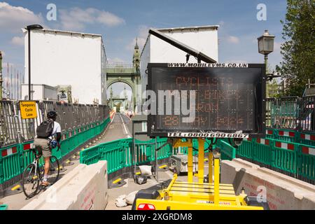 Un ciclista maschile che usa una pista ciclabile temporanea per attraversare un Hammersmith Bridge ancora chiuso nel sud-ovest di Londra, Inghilterra, Regno Unito Foto Stock