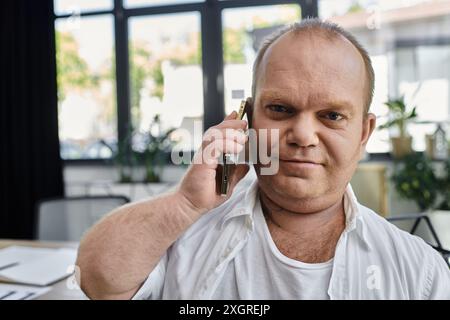 Un uomo con inclusività siede alla sua scrivania, telefonando mentre lavora nel suo ufficio domestico. Foto Stock