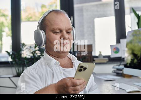 Un uomo dotato di funzionalità che indossa le cuffie e guarda il suo telefono, prendendosi un momento per rilassarsi in un ufficio affollato. Foto Stock