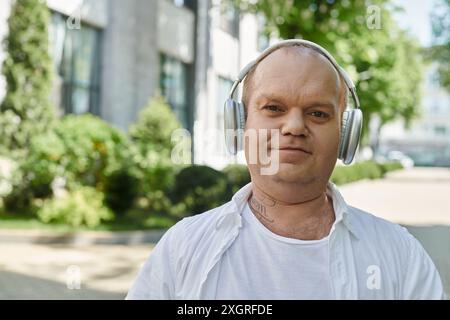 Un uomo con indosso le cuffie cammina accanto a un edificio con vegetazione sullo sfondo. Foto Stock