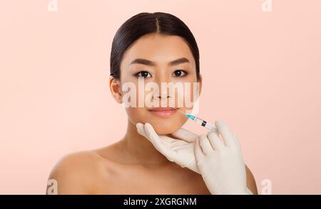 Donna che riceve iniezioni di labbra su sfondo rosa Foto Stock