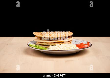 Un delizioso panini servito con un lato di cavolo, cetriolo e pomodoro su un tavolo di legno su sfondo nero Foto Stock