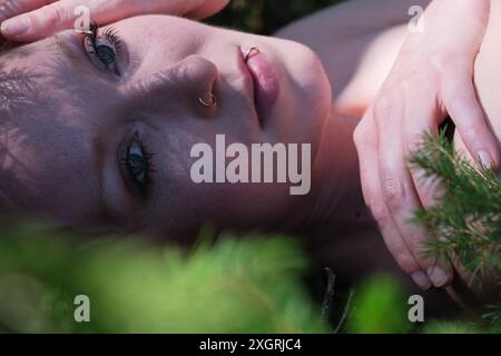 primo piano del viso sereno di una donna adagiato tra il verde del fogliame, con delicate ombre gettate dalle foglie. La sua espressione è calma e introspettiva, Captu Foto Stock