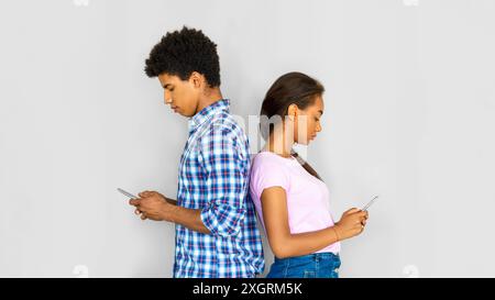Una coppia di giovani che usa gli smartphone uno contro l'altro contro il Grey Wall Foto Stock