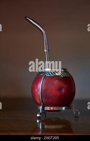 primo piano di un compagno rosso con bombilla in acciaio e dettagli in argento su un tavolo in legno, messa a fuoco selettiva. Foto Stock