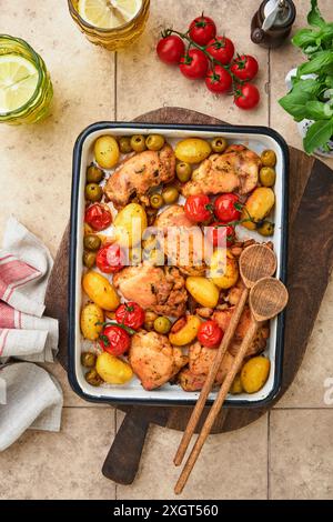 Cosce di pollo cotte con patate novelle, pomodori ciliegini e olive al vino bianco in stile borgognone in rustico piatto da forno e sfondo in legno. Coperchio o ar Foto Stock