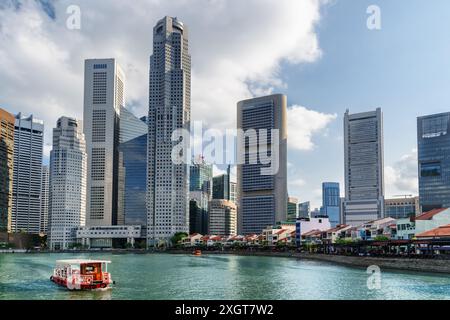 Barca turistica tradizionale a vela lungo Boat Quay con acqua azzurra a Singapore. Splendidi edifici moderni sono visibili sullo sfondo blu del cielo. Foto Stock