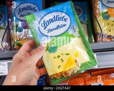 Baviera, Germania - 10 luglio 2024: Il cliente ha in mano una confezione di formaggio Landliebe dallo scaffale refrigerato di un supermercato alimentare *** Kunde hält eine Packung Landliebe Käse aus dem Kühlregal in einem Lebensmittel Supermarkt Foto Stock