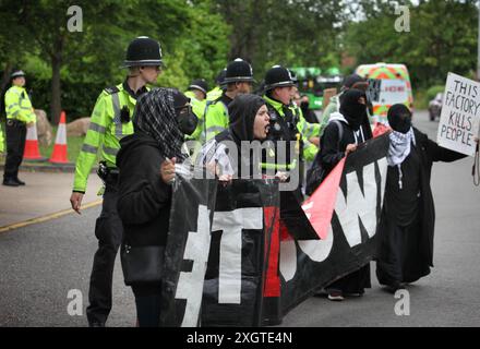 Leicester, Leicestershire, Regno Unito. 10 luglio 2024. Gli agenti di polizia formano un cordone all'ingresso della fabbrica mentre i manifestanti tengono uno striscione con scritto "Chiudi Elbit" durante la dimostrazione. I manifestanti si riuniscono fuori dalle porte della fabbrica Elbit System a Leicester per protestare mentre i lavoratori vengono a lavorare presso la compagnia israeliana di armi. I manifestanti protestano contro le armi fabbricate in questa fabbrica che ritengono vengano successivamente utilizzate per opprimere i palestinesi a Gaza e altrove. Il 85% della flotta israeliana di droni è fornito da Elbit Systems e i manifestanti vogliono le loro sette attività rimanenti Foto Stock