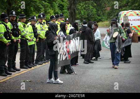 Leicester, Leicestershire, Regno Unito. 10 luglio 2024. Gli agenti di polizia formano un cordone all'ingresso della fabbrica mentre i manifestanti tengono uno striscione con scritto "Chiudi Elbit" durante la dimostrazione. I manifestanti si riuniscono fuori dalle porte della fabbrica Elbit System a Leicester per protestare mentre i lavoratori vengono a lavorare presso la compagnia israeliana di armi. I manifestanti protestano contro le armi fabbricate in questa fabbrica che ritengono vengano successivamente utilizzate per opprimere i palestinesi a Gaza e altrove. Il 85% della flotta israeliana di droni è fornito da Elbit Systems e i manifestanti vogliono le loro sette attività rimanenti Foto Stock