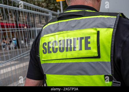 Gilet giallo fluorescente con la parola "sicurezza" scritta in francese sul retro e indossata da una guardia di sicurezza privata che guarda un sito sicuro Foto Stock