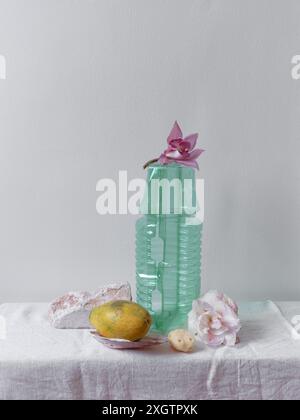 Un allestimento minimalista di STILL Life caratterizzato da una plastica verde con un'orchidea rosa, accompagnata da un frutto e alcune pietre decorative su un coagulo di lino testurizzato Foto Stock