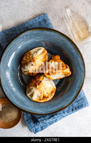 I tradizionali gnocchi georgiani, i khinkali, sono perfettamente cucinati e serviti in una ciotola di ceramica blu stilizzata su un panno di denim, con uno sfondo sottile Foto Stock