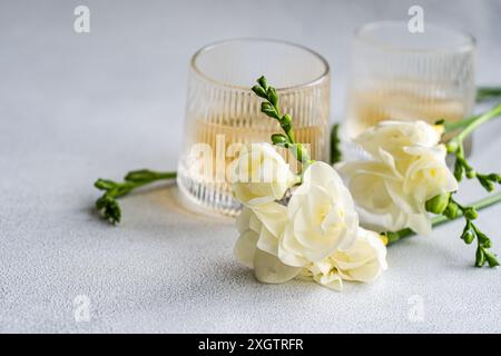 Un'immagine sofisticata che mostra un cocktail di vodka alla pesca in un vetro a costine, completato da delicati fiori bianchi di Freesia, adagiati su un grigio testurizzato Foto Stock