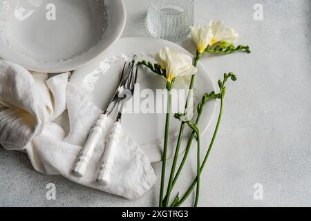 Un sofisticato tema del tavolo caratterizzato da delicati fiori Freesia bianchi, piatti eleganti e posate in argento con manici bianchi, completate da un Foto Stock