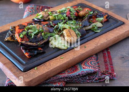 Colorato mix di verdure alla griglia, tra cui melanzane, peperoni e funghi, guarnite con erbe fresche su un tavolo da portata in legno Foto Stock