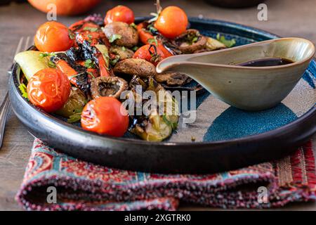 Una vivace insalata di verdure alla griglia con pomodori ciliegini affumicati, funghi, peperoni e lattuga servita in un'elegante ciotola in ceramica accompagnata da un Foto Stock