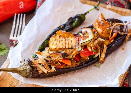 Melanzane ripiene al forno con pomodori ciliegini, peperoni, cipolla, aglio, fette sottili di patate, formaggio e microgreen serviti su carta pergamena." Foto Stock