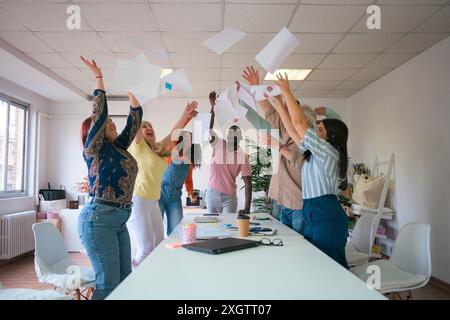 Un gruppo eterogeneo di colleghi che celebrano il successo lanciando con gioia i documenti in aria, catturando un momento di lavoro di squadra e felicità in una Foto Stock