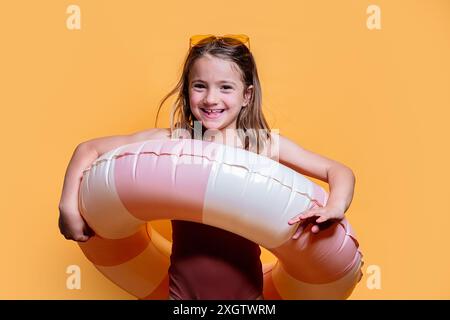 Una ragazza allegra posa con un anello gonfiabile rosa su uno sfondo giallo vibrante, catturando l'essenza dell'estate il suo sorriso radioso e il suo sporco Foto Stock