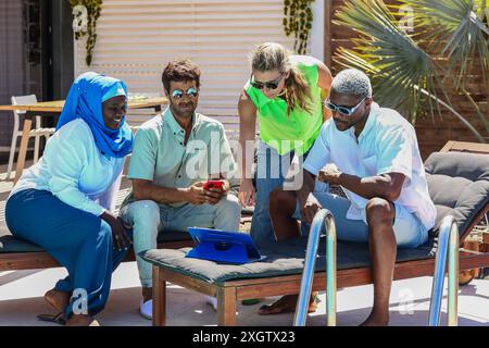 Un gruppo multietnico di quattro adulti si impegna in una discussione di lavoro all'aperto durante l'estate. Una donna musulmana in un hijab, un uomo caucasico e due Africa Foto Stock