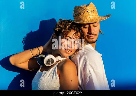 Una donna e un uomo caucasici abbracciano da vicino uno sfondo blu vivido. La donna, adornata di capelli ricci e un naso perforante, guarda in basso mentre riposa Foto Stock