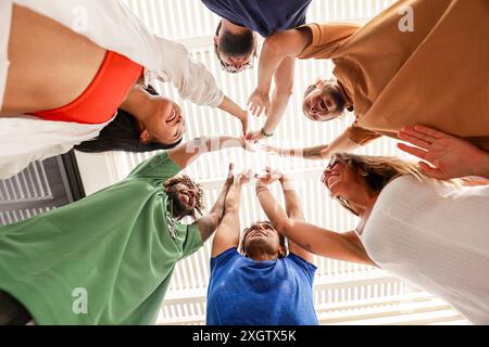 Un gruppo eterogeneo di amici che formano un cerchio e danno a un gruppo cinque alti, visti da un angolo basso su uno sfondo luminoso. Il gruppo include uomini Foto Stock