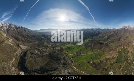 Paesaggio panoramico di lussureggianti vallate verdi circondate da torreggianti montagne con cime innevate sotto un cielo azzurro, attraversate da strade tortuose e. Foto Stock