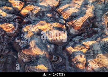 Un'immagine accattivante che mostra i motivi intricati e colorati delle formazioni di argilla bentonite illuminate dal caldo bagliore del sole che tramonta. Questo Foto Stock