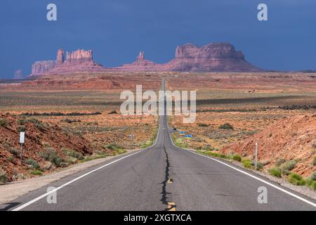 Vista panoramica di una strada rettilinea che si estende verso le iconiche arenarie rosse della Monument Valley, situata al confine tra Arizona e Utah sotto un trasparente Foto Stock