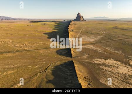 Ripresa aerea dell'impressionante Shiprock, iconica formazione rocciosa del New Mexico, che getta una lunga ombra sul vasto e arido paesaggio durante l'ora d'oro. Foto Stock