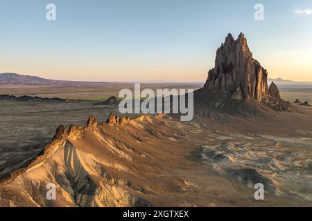 Vista panoramica dell'iconica formazione rocciosa di Shiprock inondata dalla luce dorata del tramonto su un vasto paesaggio desertico nel New Mexico, Stati Uniti. Foto Stock